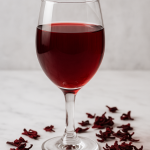 Glass of homemade hibiscus wine with dried hibiscus petals on a table