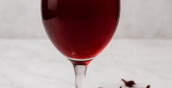 Glass of homemade hibiscus wine with dried hibiscus petals on a table